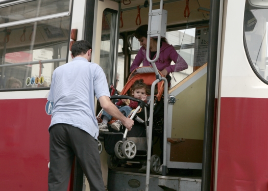 Ein Straßenbahnfahrer hilft einer Mutter mit Kinderwagen beim Aussteigen einer Straßenbahn.