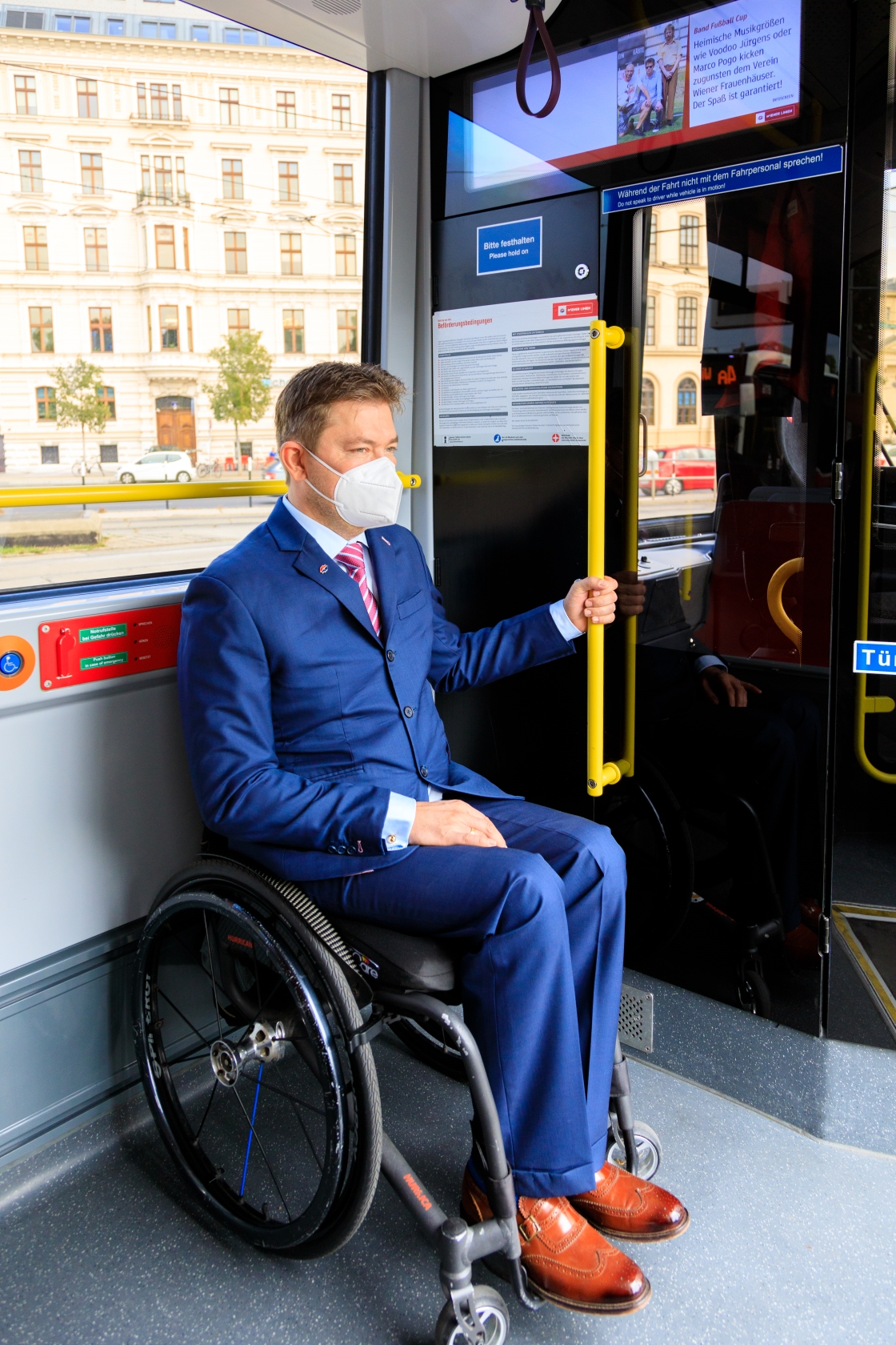 Ein Fahrgast im Rollstuhl steht am Platz für Rollstuhlbenutzer*innen in einer Straßenbahn.