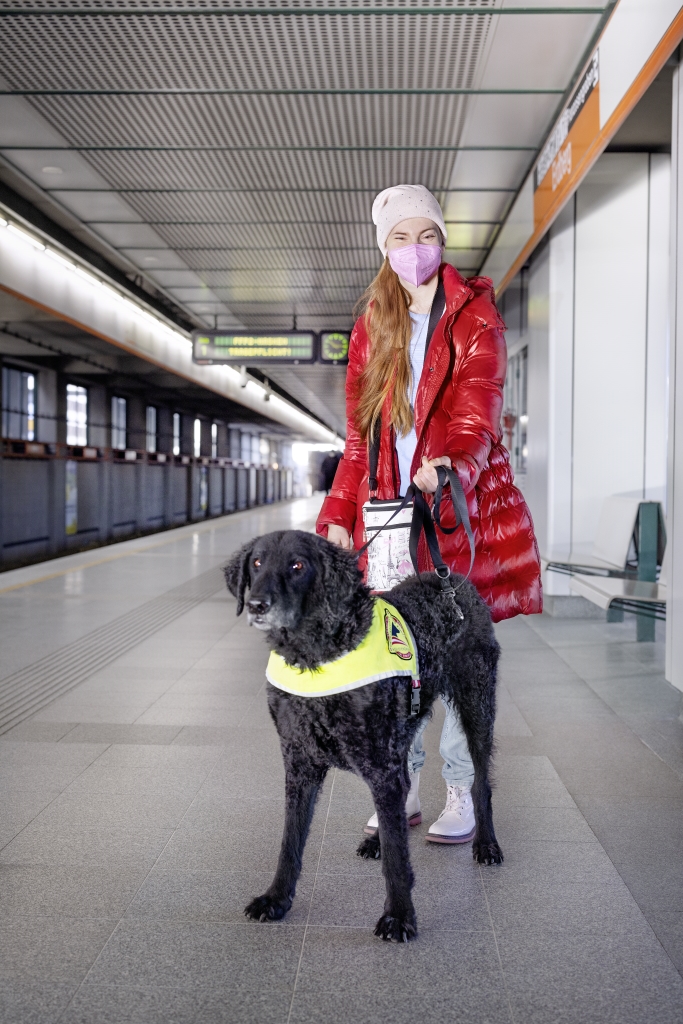 Ein weiblicher Fahrgast mit ihrem Assistenzhund. Der Hund ist mit dem typischen gelben Tuch gekennzeichnet.